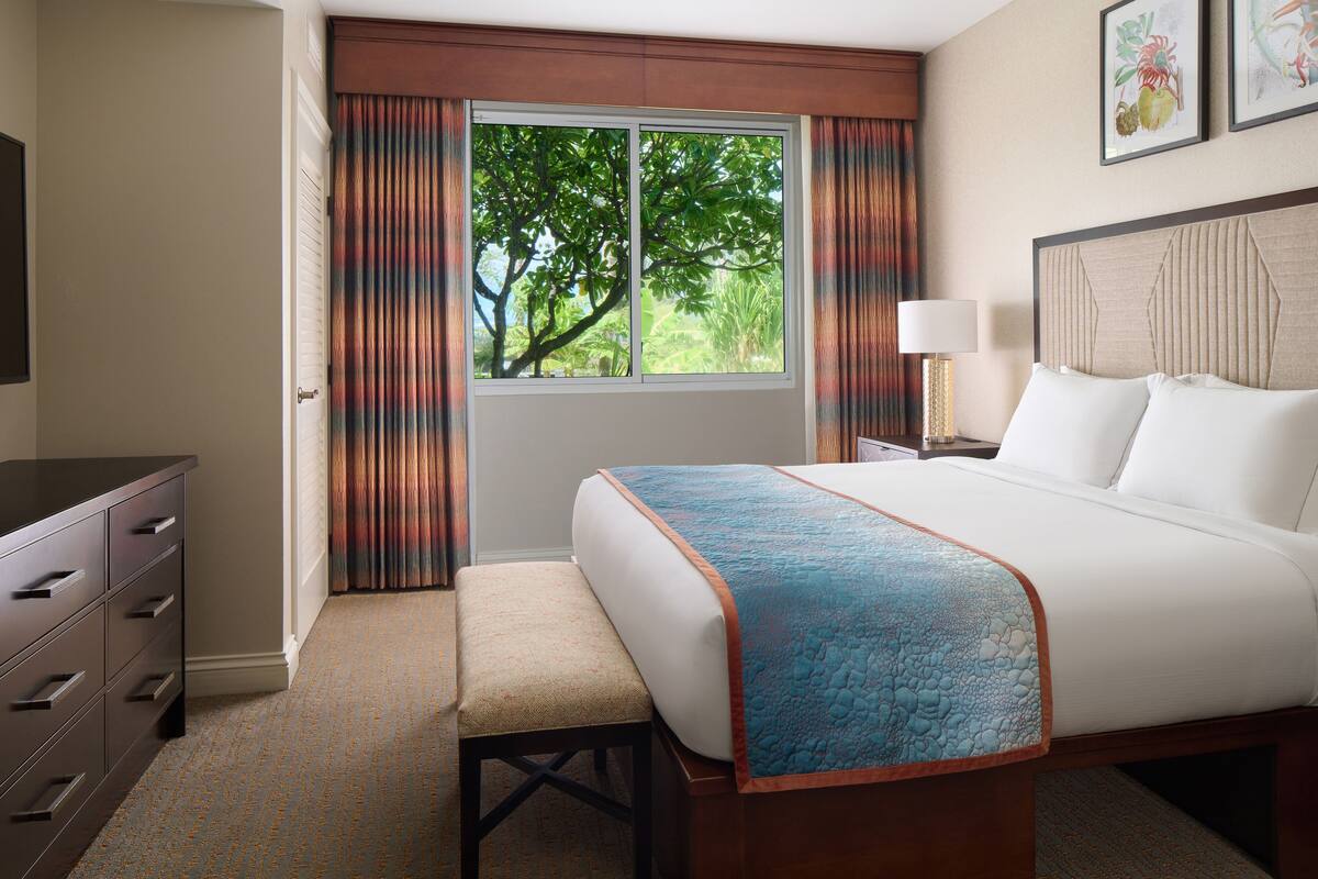 Une chambre d’hôtel avec un lit, un bureau, une chaise, une fenêtre avec des rideaux et une lampe.