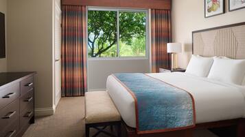 A hotel room with a bed, a desk, a chair, a window with curtains, and a lamp.