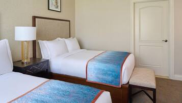 A hotel room with two beds, a nightstand with a lamp, a door, and a framed picture on the wall.
