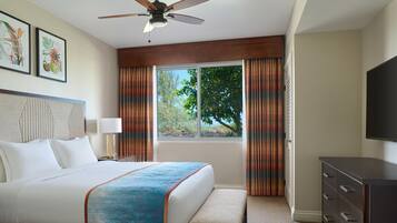 A hotel room with a bed, a desk, a chair, a TV, a window with curtains, and a ceiling fan.