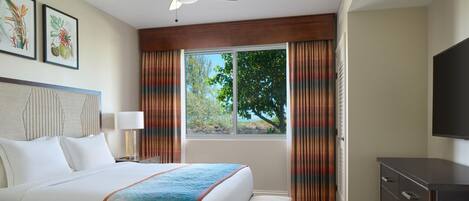 A hotel room with a bed, a desk, a chair, a TV, a window with curtains, and a ceiling fan.