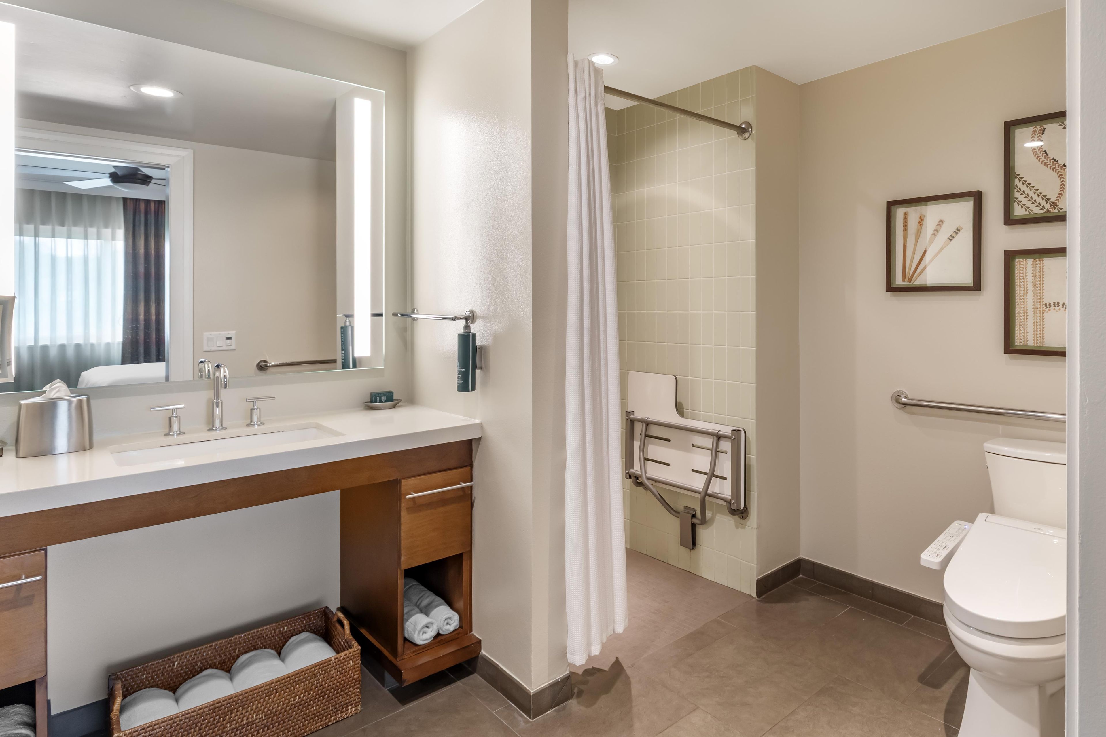 A modern bathroom with a large mirror, a sink with a towel rack, a shower with a grab bar, and a toilet.