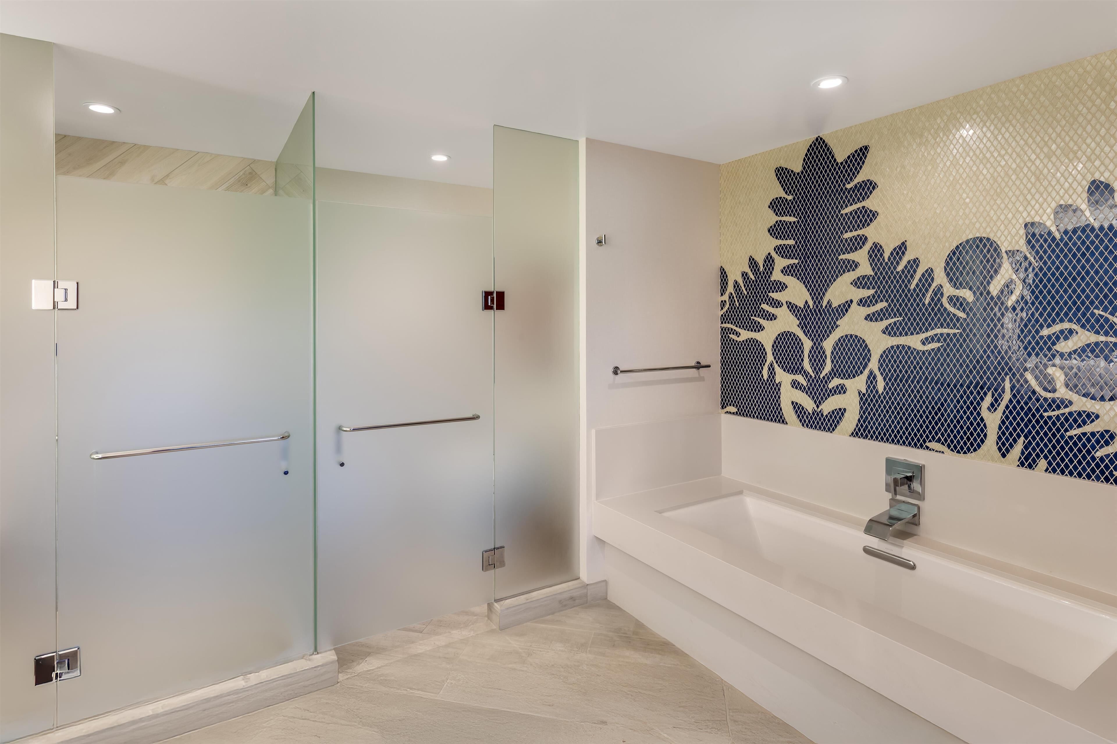 Une salle de bain moderne avec une douche à l’italienne en verre, une baignoire blanche et un mur décoratif orné de motifs de feuilles.