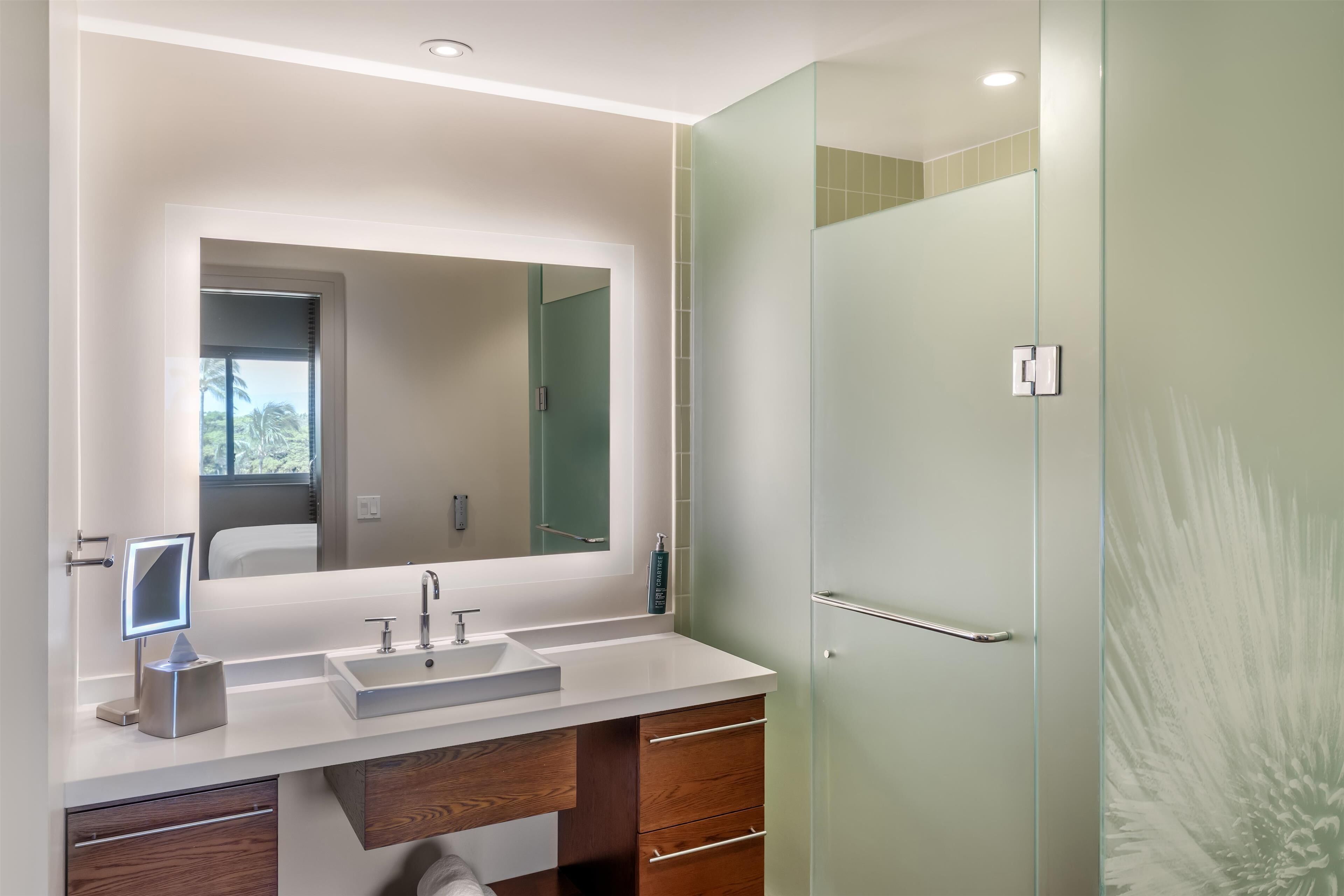 Un baño moderno con un espejo grande, un lavabo y una cabina de ducha de vidrio.