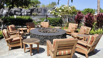 An outdoor seating area with a circular fire pit surrounded by striped chairs and tables.