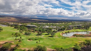Un parcours de golf comprenant plusieurs bâtiments, un étang et un paysage montagneux en arrière-plan.