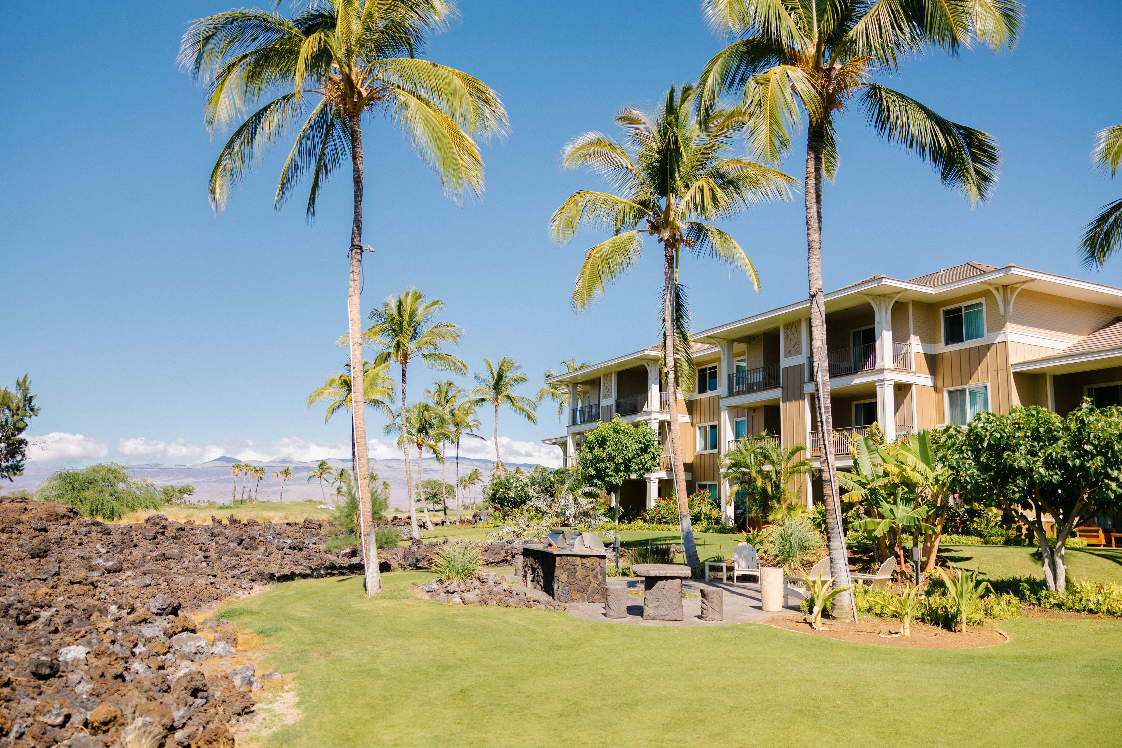 A hotel with multiple floors, a well-maintained lawn, and several palm trees.