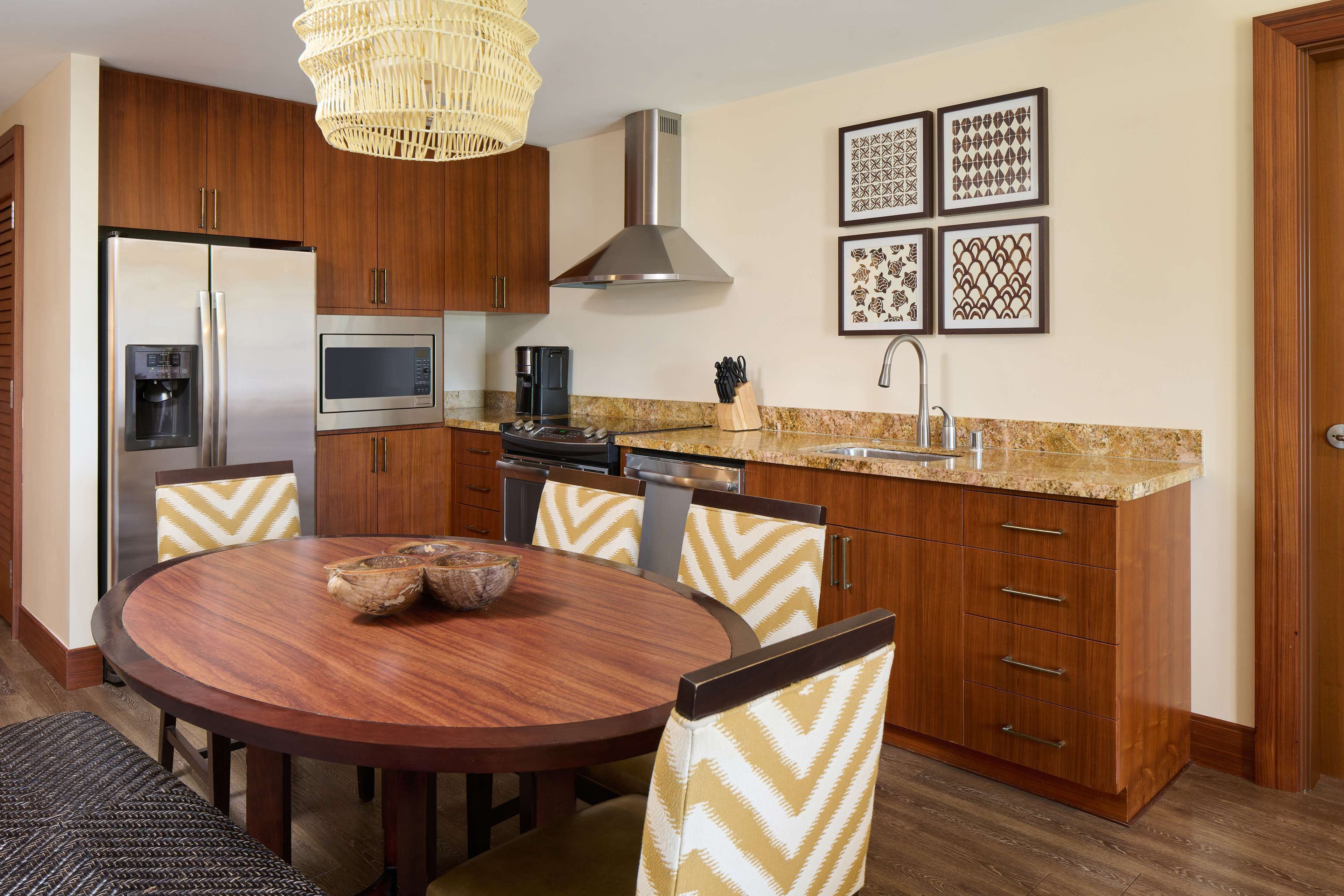 A modern kitchen with wooden cabinets, stainless steel appliances, a round dining table, and patterned chairs.