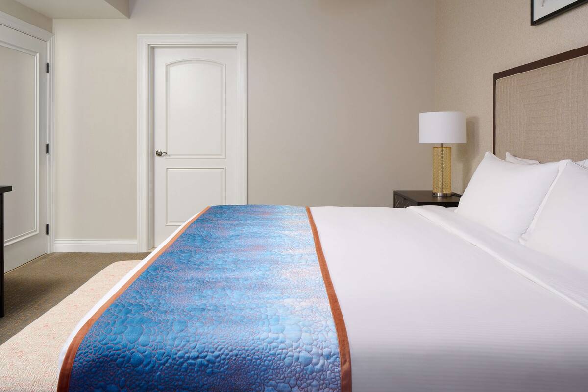 Une chambre d’hôtel avec un lit, une table de chevet, une lampe et une porte.