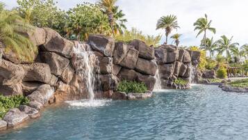 Formación rocosa natural con cascada que desemboca en una piscina cristalina, rodeada de exuberante vegetación tropical.