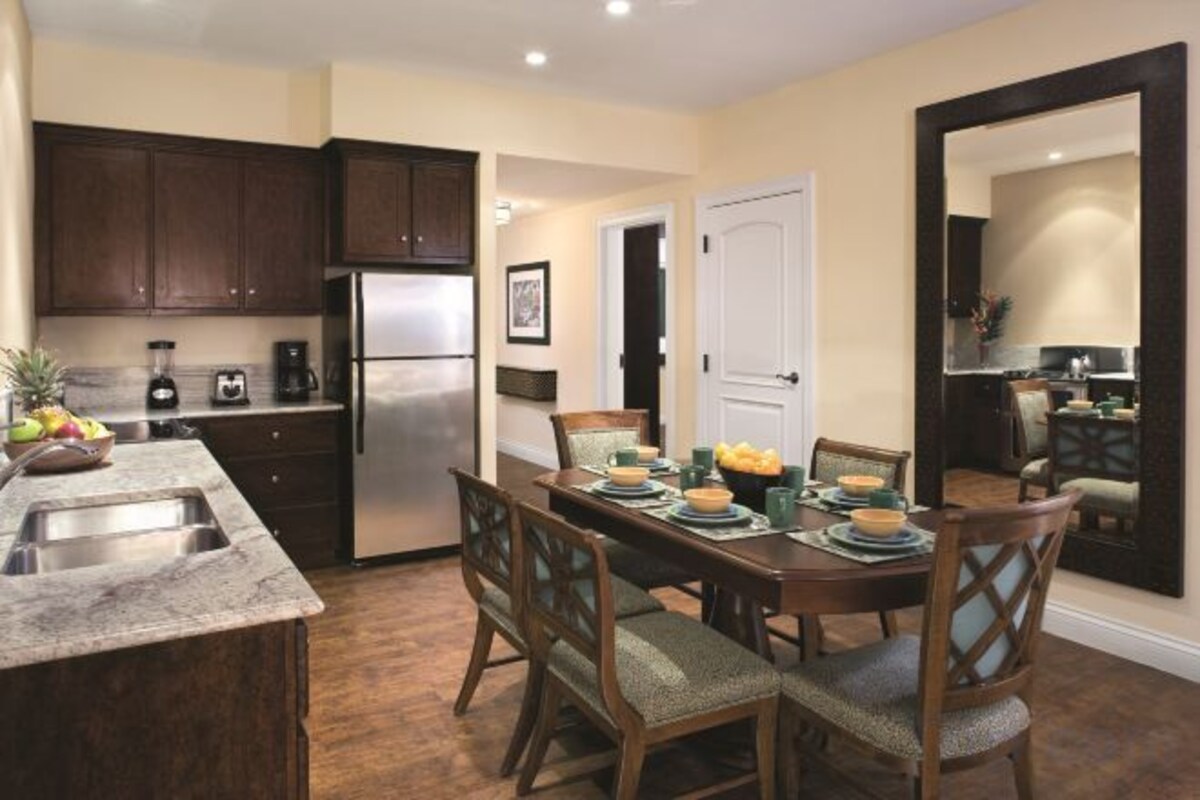 A kitchen with dark wood cabinets, a stainless steel refrigerator, and a dining area with a wooden table and chairs.
