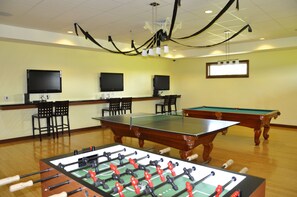 Une pièce équipée d’un baby-foot, d’une table de billard et de deux téléviseurs fixés au mur.
