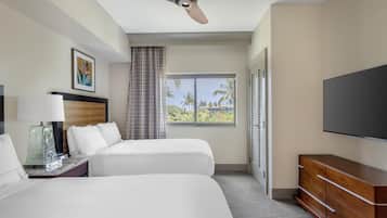 Habitación de hotel con cama, televisor, escritorio con lámpara y ventana con vista a palmeras.