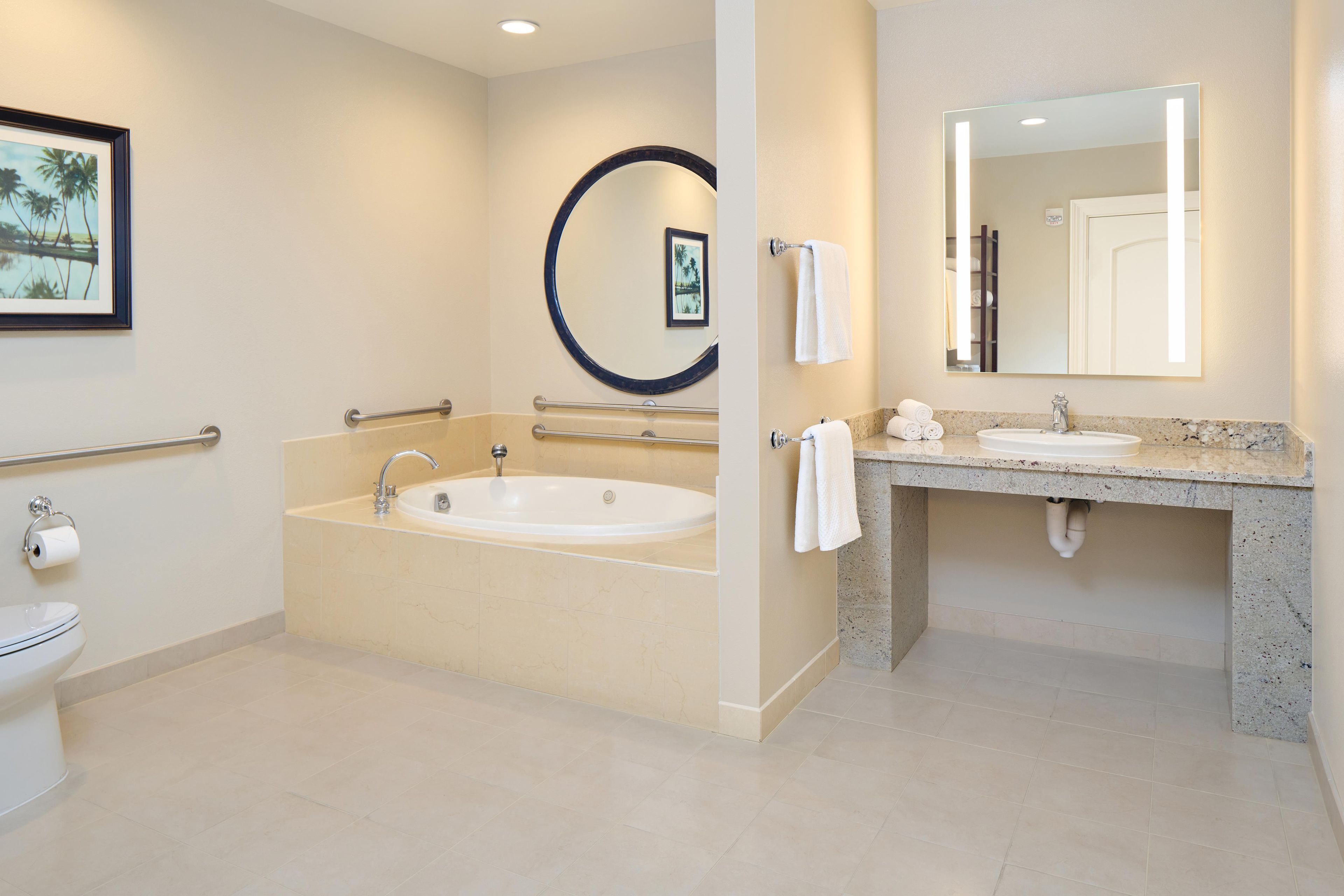 A modern bathroom with a bathtub, a sink, and a toilet. There are handrails and a towel rack.