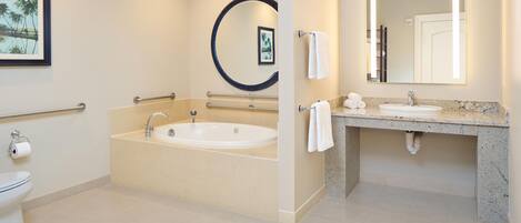 A modern bathroom with a bathtub, a sink, and a toilet. There are handrails and a towel rack.