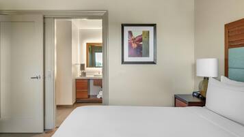 A hotel room with a bed, a nightstand with a lamp, a framed picture on the wall, and a bathroom visible through an open door.