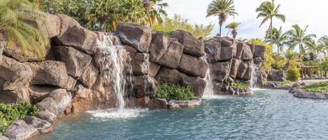 A waterfall cascading over rocks into a pool surrounded by palm trees.