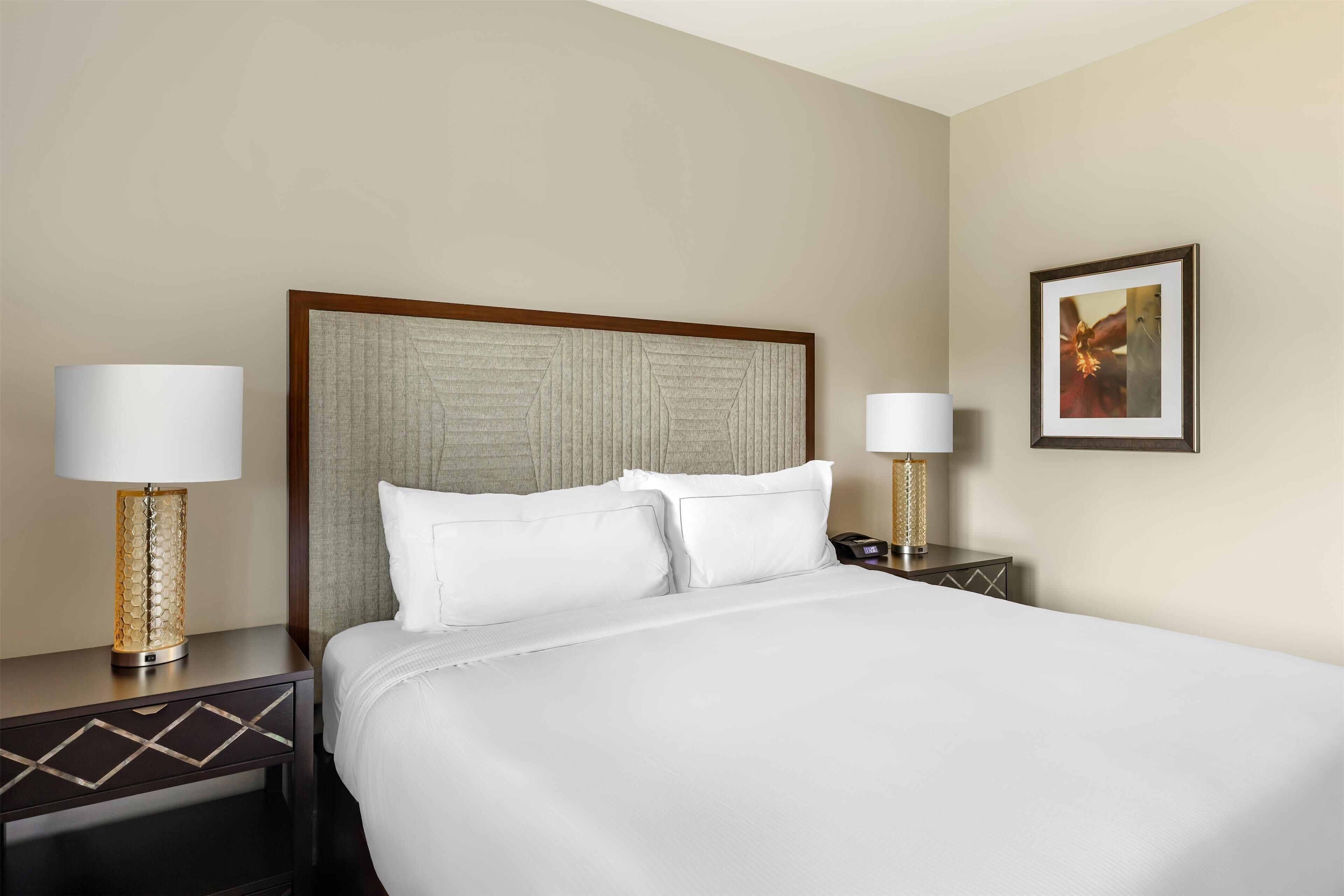 A hotel room with a large bed, two bedside tables with lamps, and a framed picture on the wall.