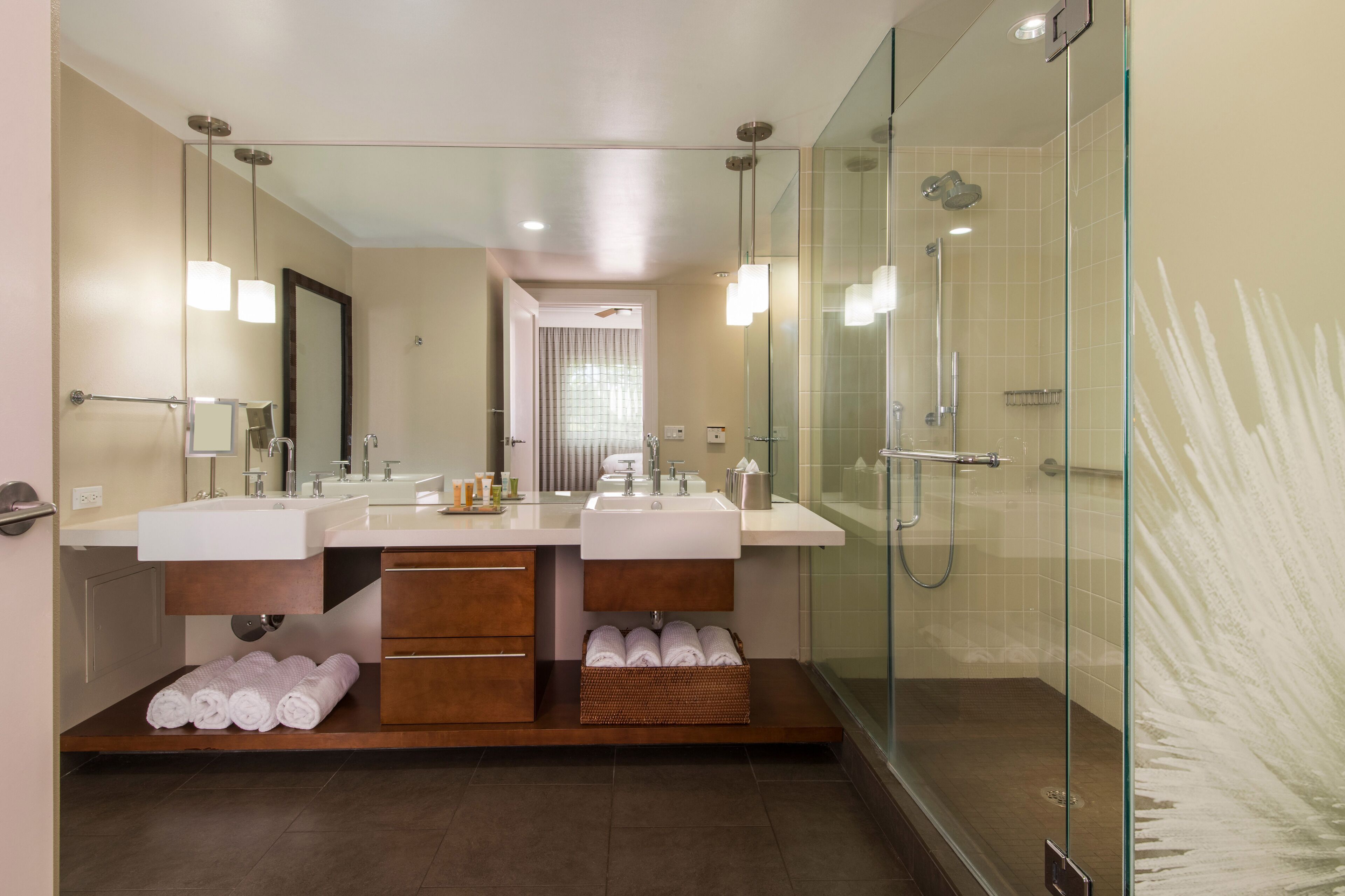 A modern bathroom with two sinks, a glass shower enclosure, and a vanity with storage drawers.