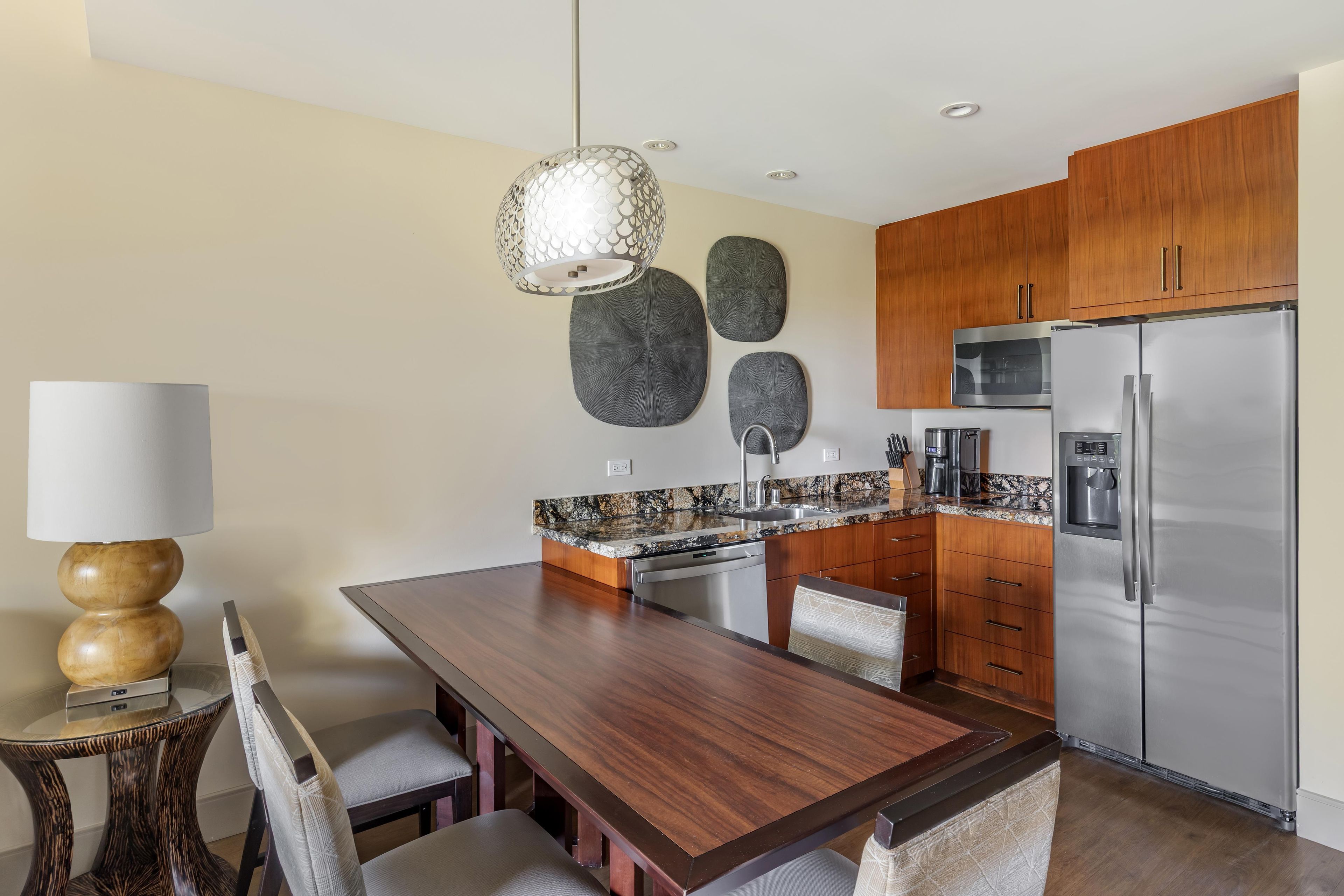 Una cocina moderna con una mesa de comedor de madera, sillas, horno empotrado y refrigerador de acero inoxidable.