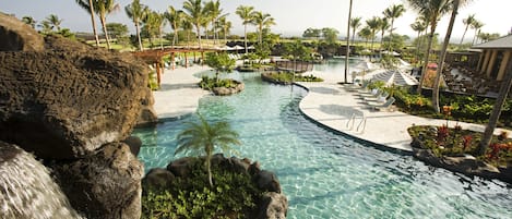 A resort pool with clear water, palm trees, and a waterfall.