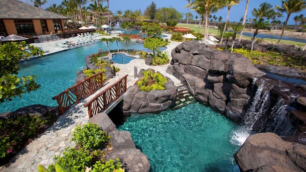 Un espace piscine d’un complexe hôtelier comprenant plusieurs piscines, une cascade et un pont en bois.