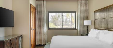 A hotel room with a large bed, a television, a window with curtains, and a ceiling fan.