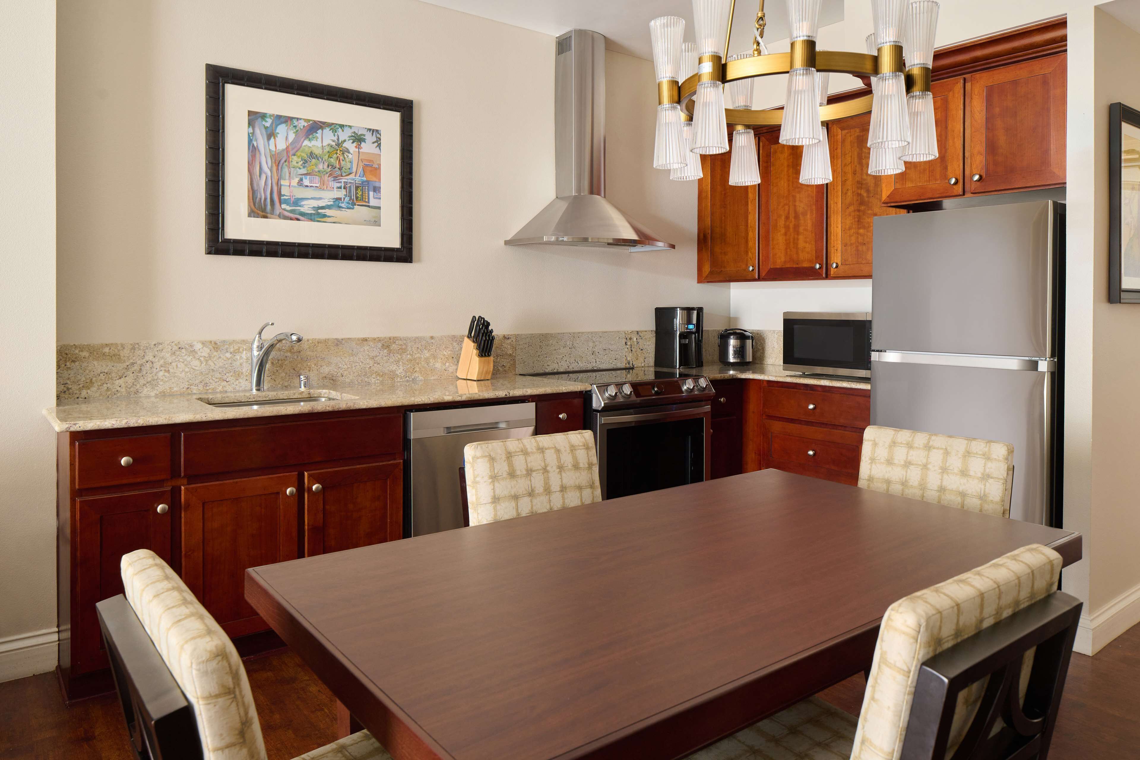 Une cuisine moderne avec des meubles en bois, un réfrigérateur en acier inoxydable, un four encastré et une table à manger avec des chaises rembourrées.