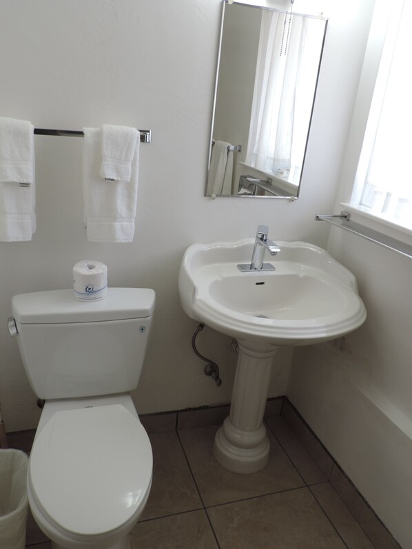 A bathroom with a toilet, sink, and mirror. - Cambria Palms Motel (Cambria)