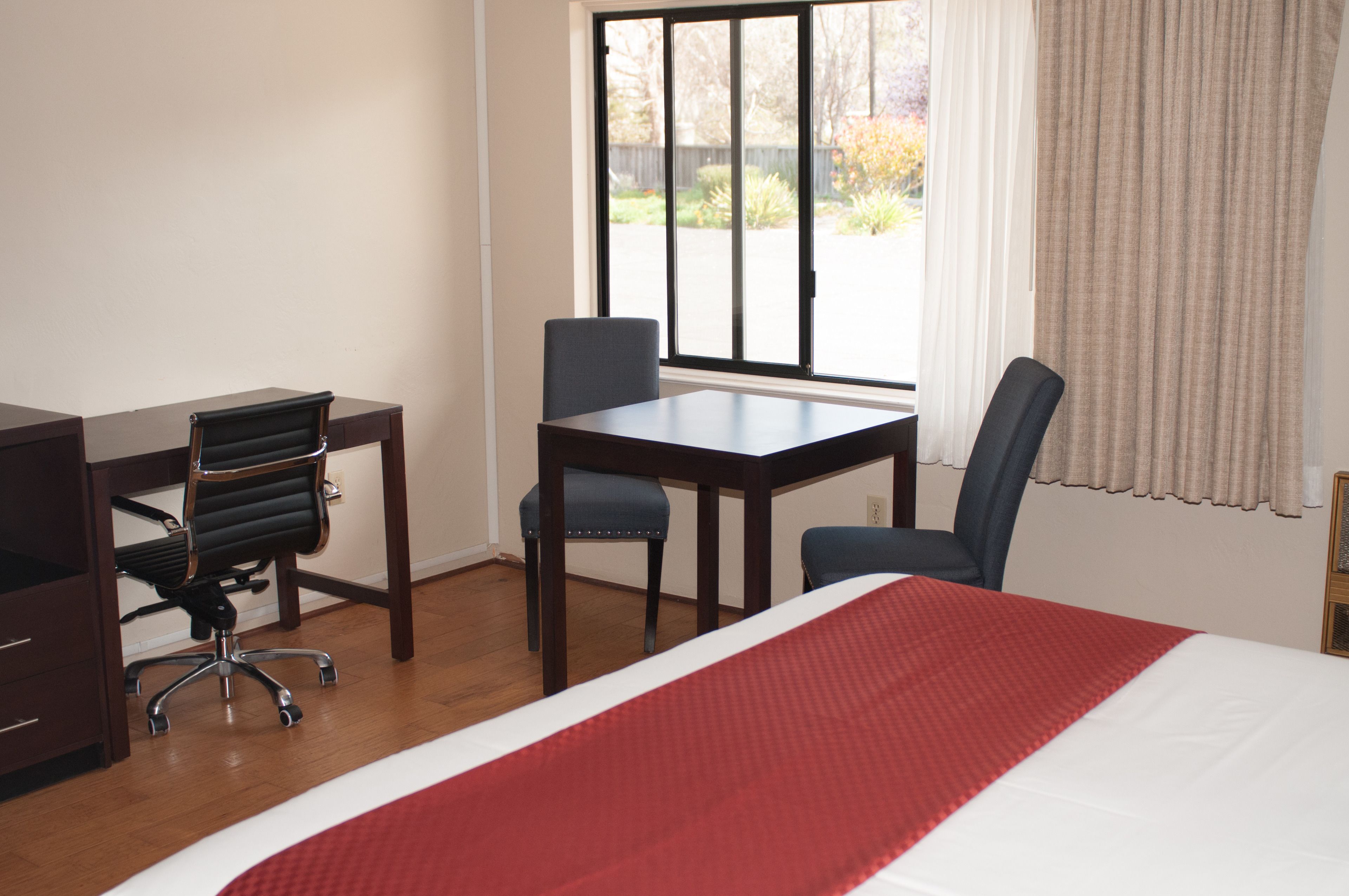 Una habitación de hotel con cama, escritorio, dos sillas y ventana con cortinas.