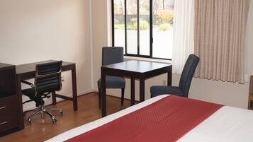 Una habitación de hotel con cama, escritorio, dos sillas y ventana con cortinas.