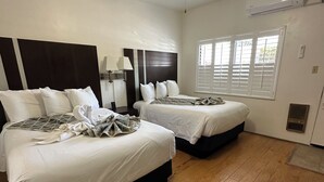 A hotel room with two beds, a ceiling fan, a window with blinds, and a wall-mounted air conditioner.