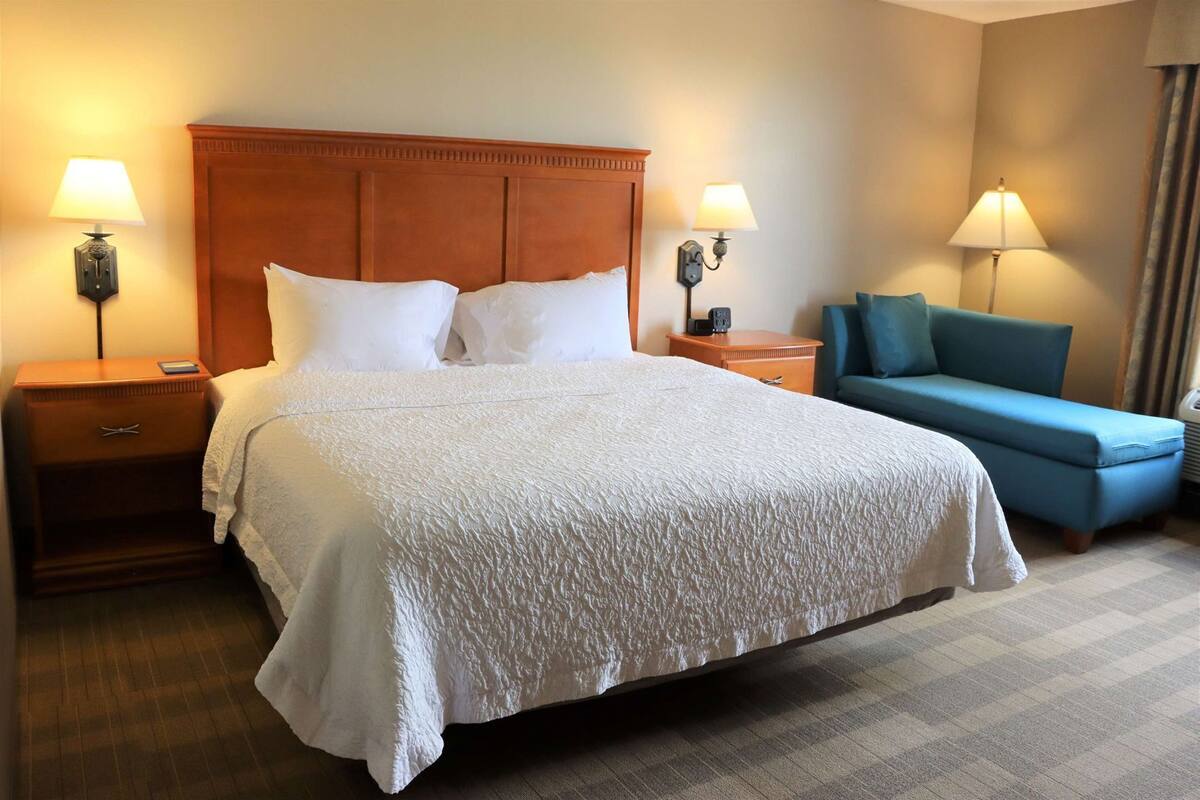 A hotel room with a large bed, two bedside tables, a blue sofa, and two wall-mounted lamps.