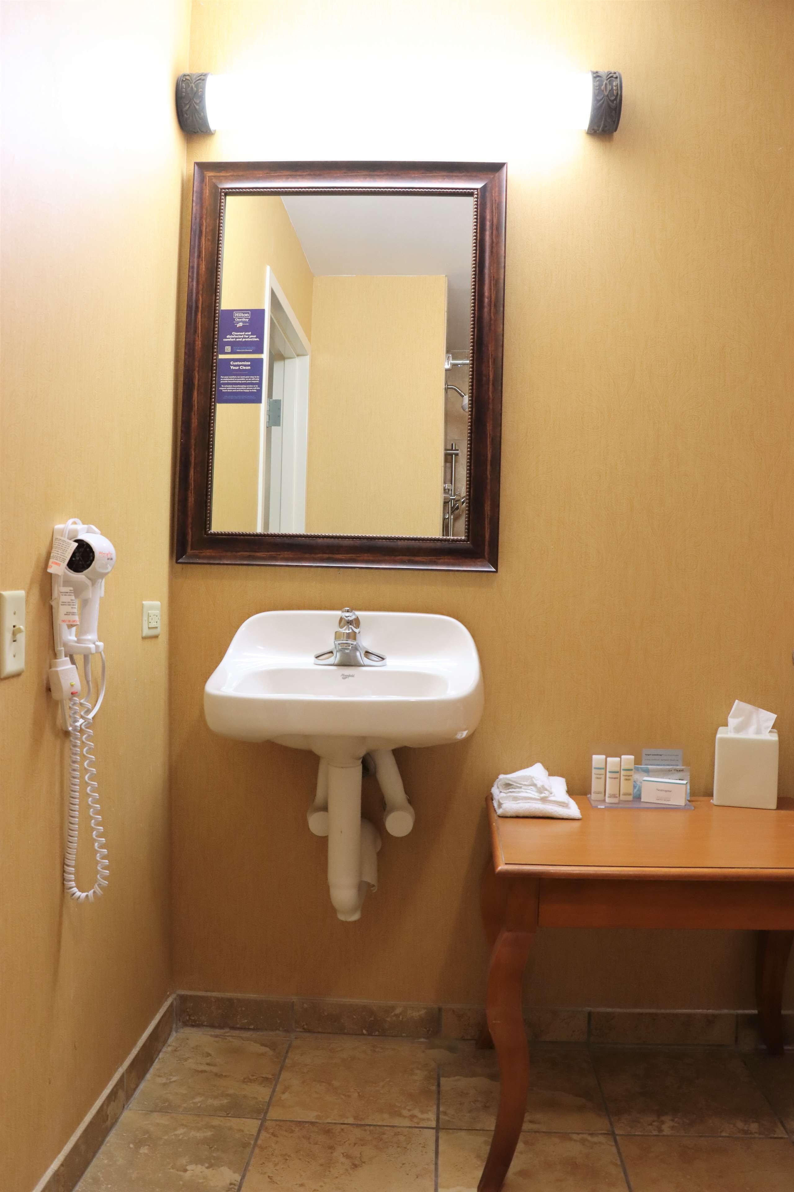 Un baño con lavamanos, espejo, secador de pelo y artículos de aseo sobre una mesa.