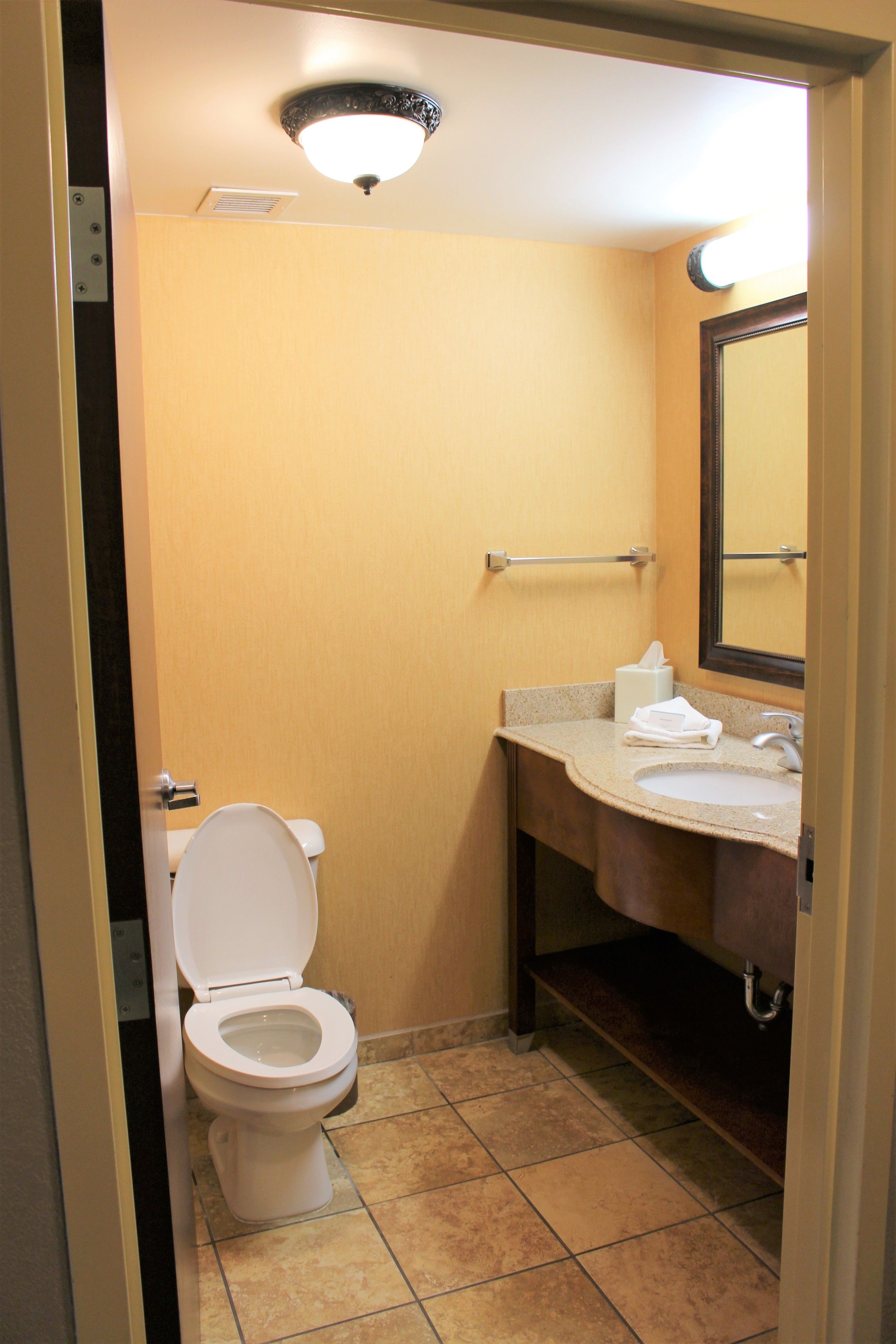 A compact hotel bathroom with a toilet, sink, and mirror.