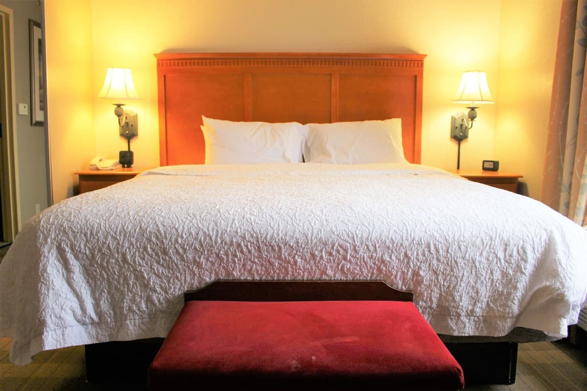 A hotel room with a large bed, two bedside lamps, a telephone, and a red bench.