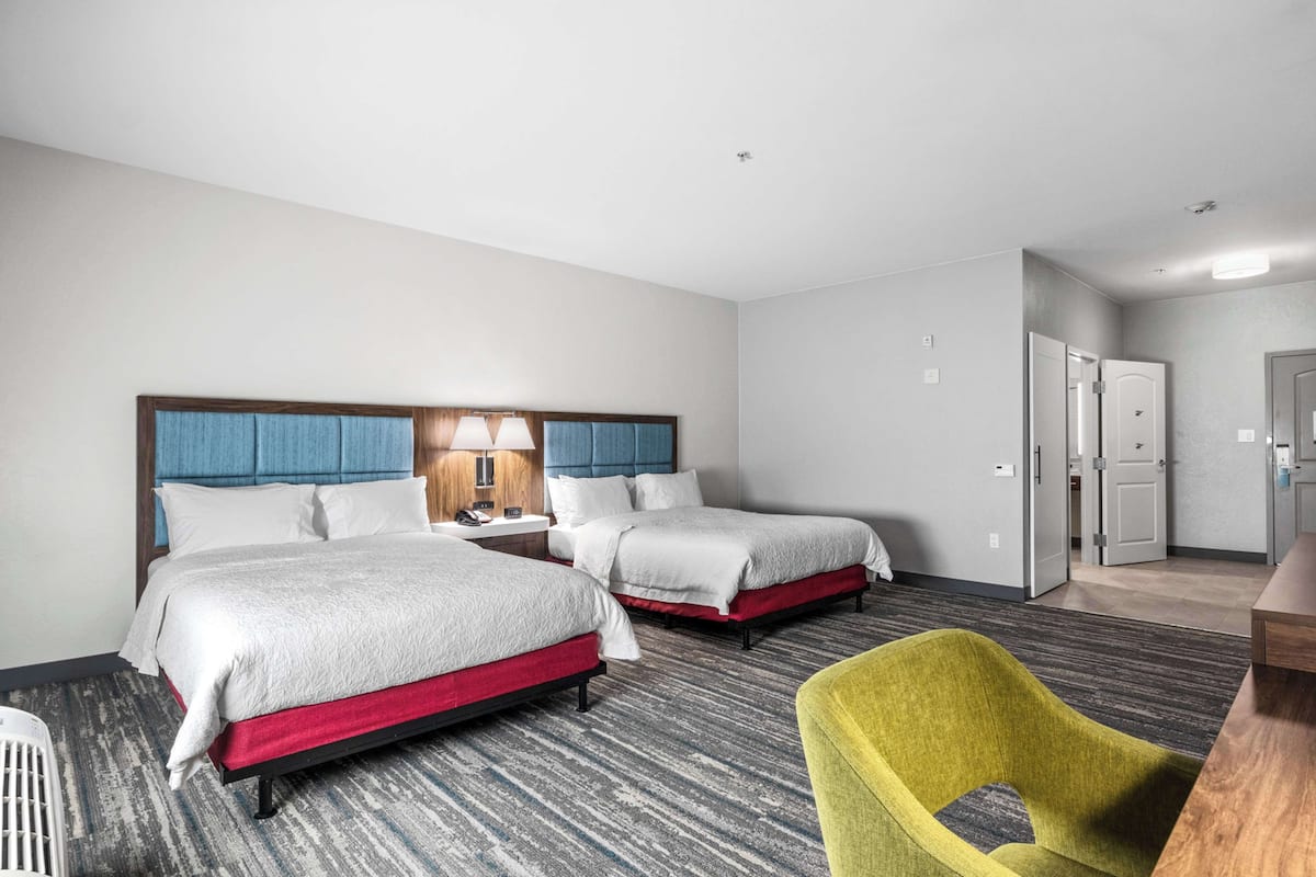 A hotel room with two beds, a desk, a chair, and a kitchenette.