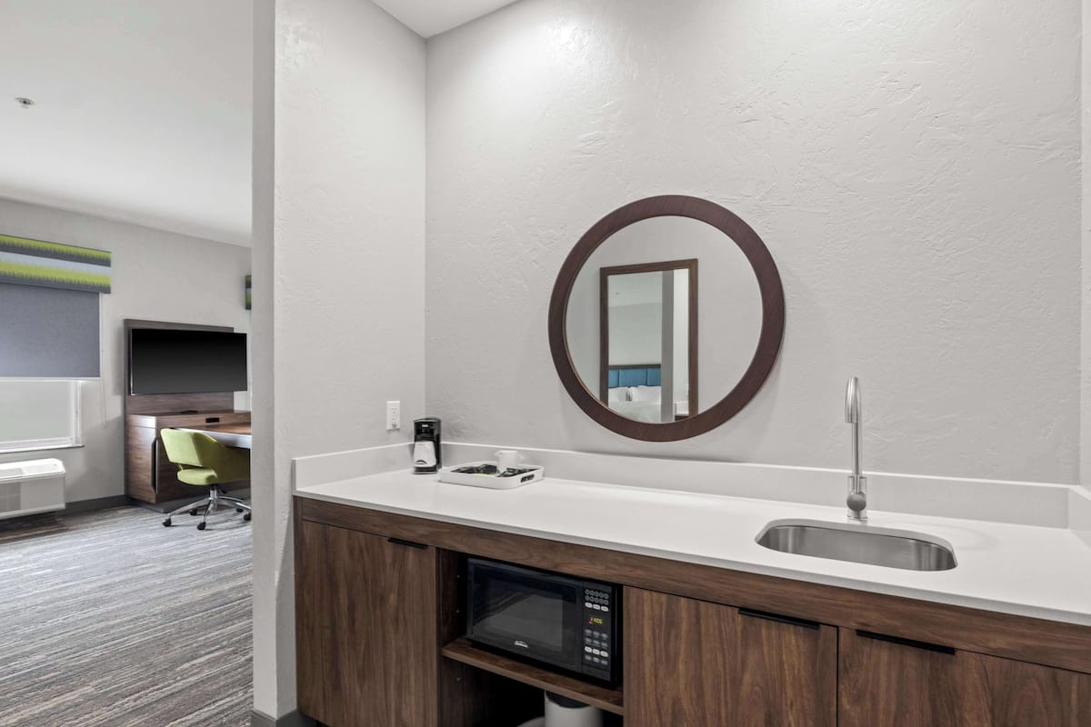A modern bathroom with a white countertop, a sink, a mirror, and a built-in microwave.