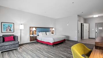 Una habitación de hotel con cama, sofá, sillón, escritorio y un cuadro en la pared.