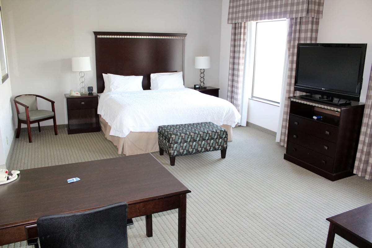A hotel room with a bed, two bedside tables with lamps, a television on a stand, a desk with a chair, and an ottoman.