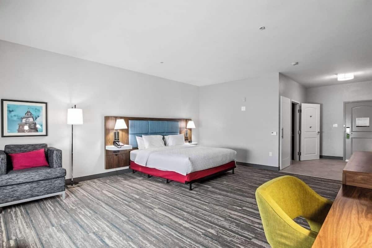 A hotel room with a bed, a sofa, a chair, a desk, and a painting on the wall.