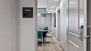 A hotel corridor with a sign reading "TITUS vacant" and a conference room with teal chairs and a patterned carpet.