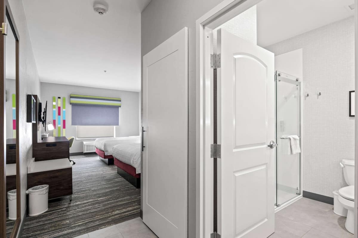 A modern hotel room with a bed, a desk, a mirror, a shower, and a toilet.