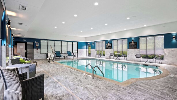 A modern indoor swimming pool with clear water, surrounded by lounge chairs and a tiled floor.