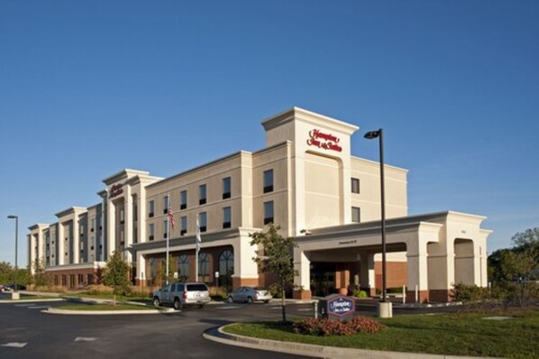 Un hotel Hampton Inn con una fachada moderna, varios accesos y un estacionamiento.