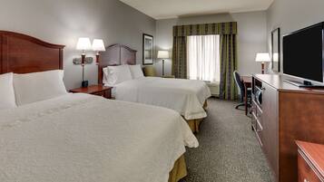 A hotel room with two beds, a desk, a television, and a window with curtains.