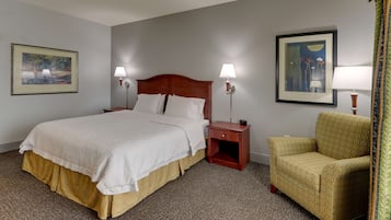 Una habitación de hotel con una cama grande, dos mesitas de noche con lámparas, una silla y dos cuadros en las paredes.