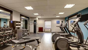 Un gimnasio con cintas de correr, mancuernas y máquinas de pesas.