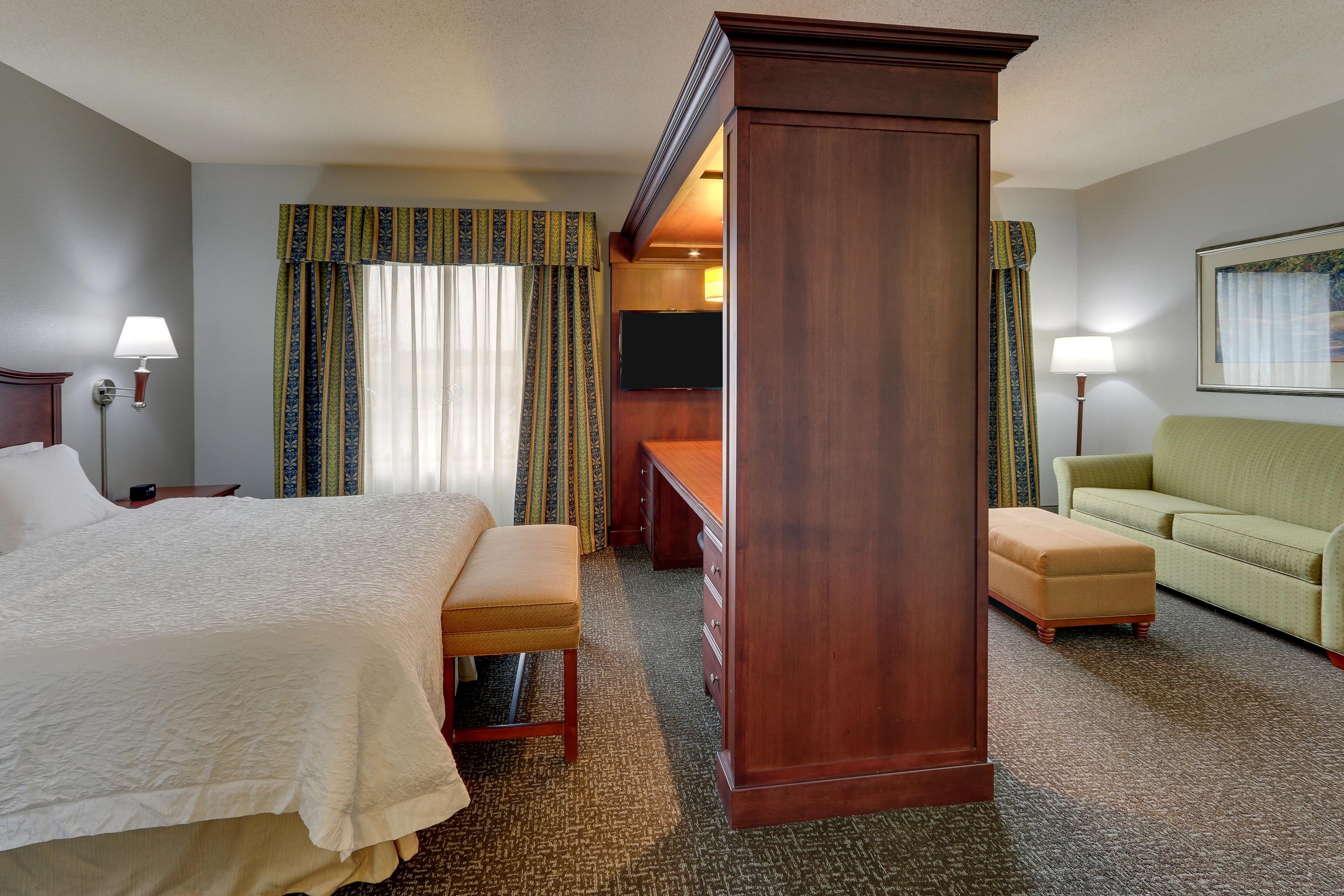 A hotel room with a large bed, a desk, a chair, a sofa, and curtains.