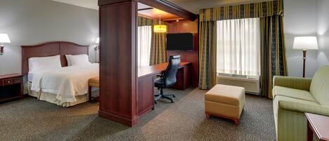 Una habitación de hotel con cama extragrande, escritorio, silla, reposapiés y televisor.
